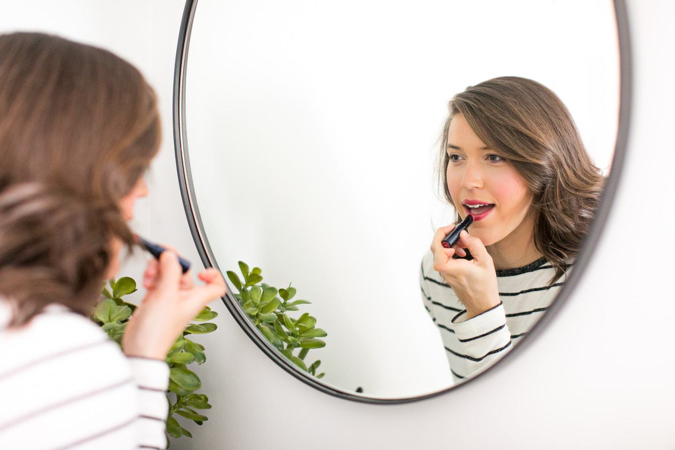 Woman looking into the mirror putting on lipstick.