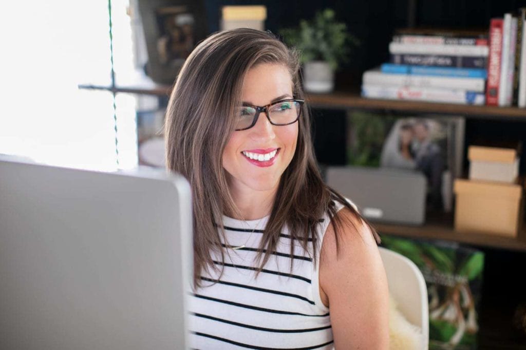 Woman in glasses in front of computer screen looking off to the side