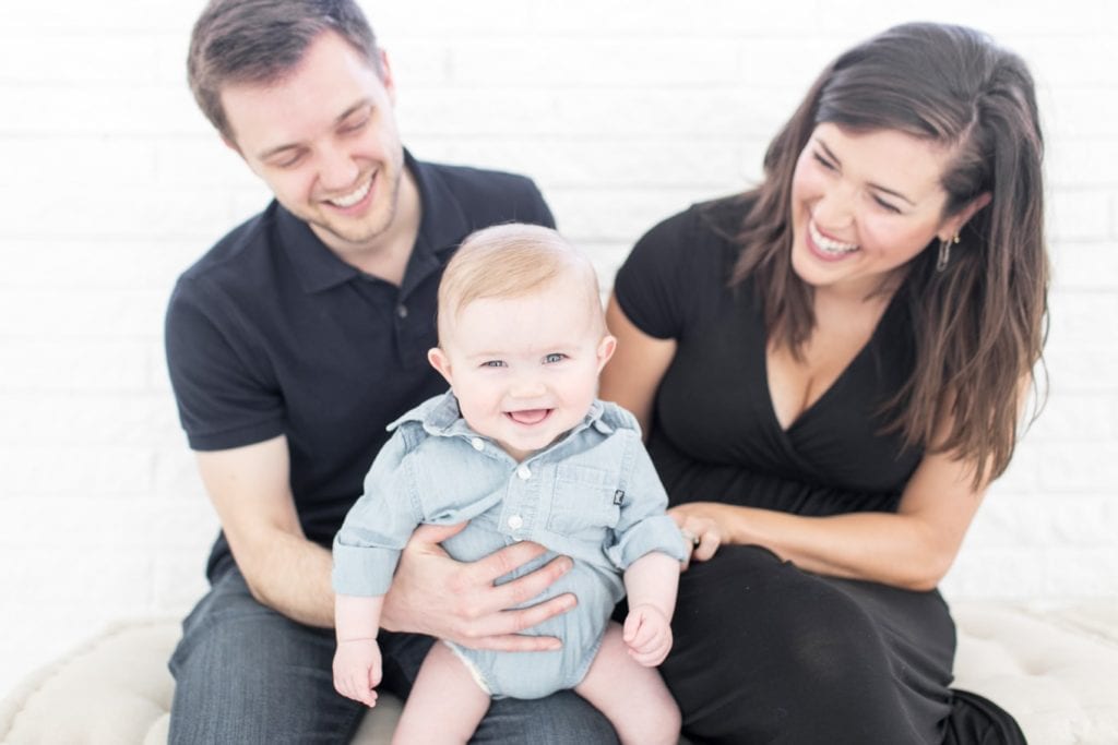 Kate Kordsmeier and family; a woman in a black dress, a man in a navy polo shirt and jeans, and a baby boy all sitting down together and smiling