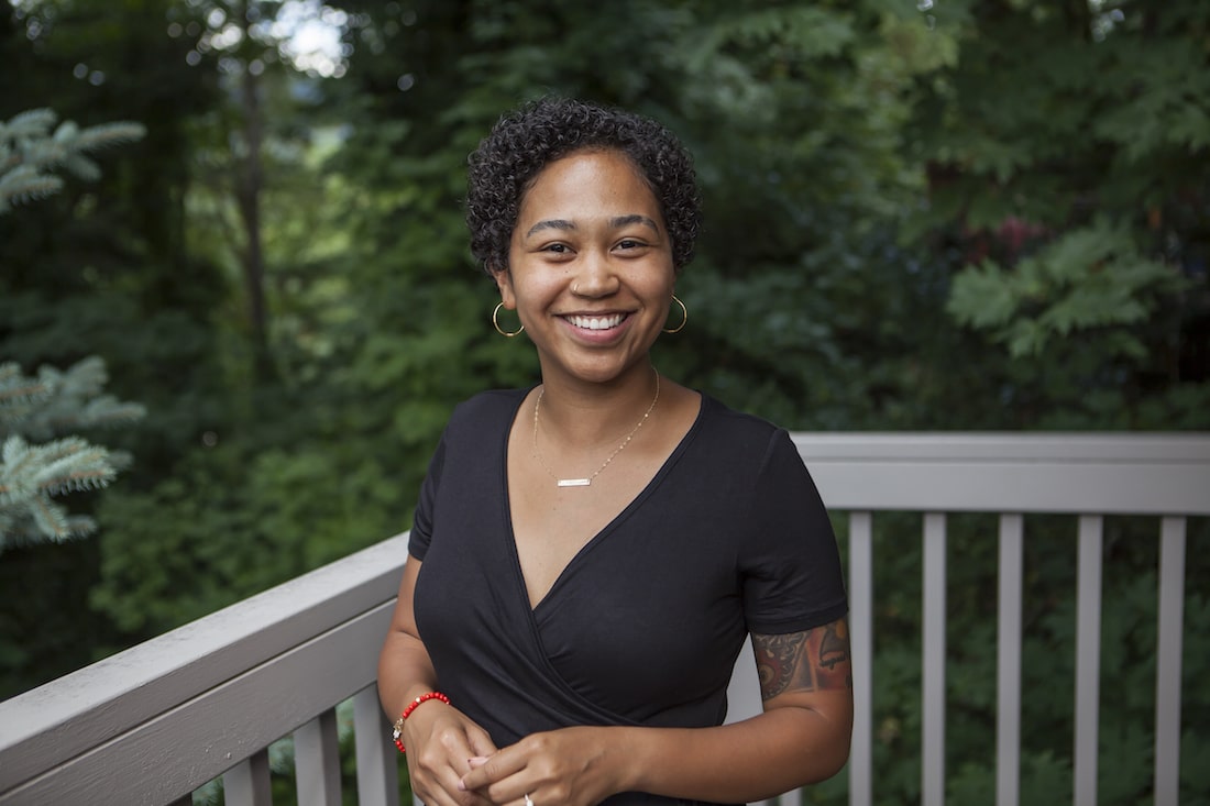 Black woman with short hair smiling on a deck in a black dress