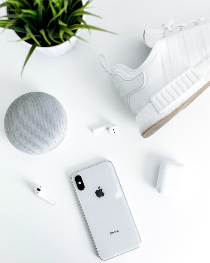 A white table with a white iphone, white headphones, speakers, shoe, and a plant