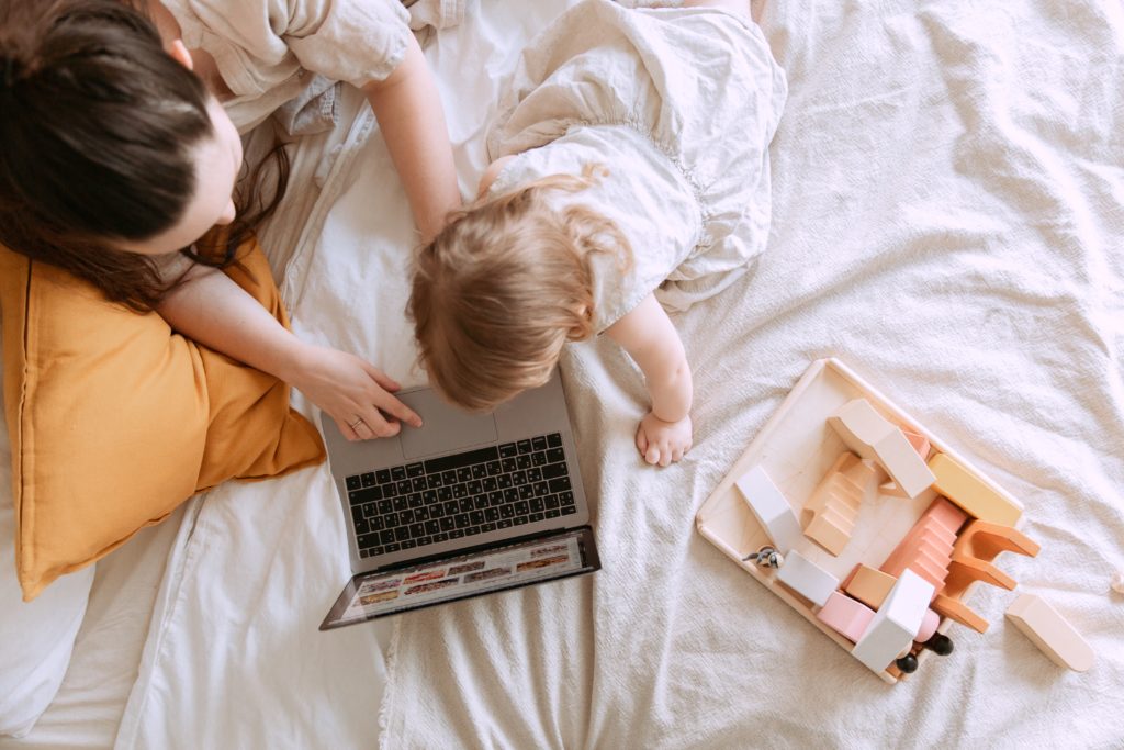 Birds-eye-view of a woman laying on a bed with her baby, her laptop in front of them. 