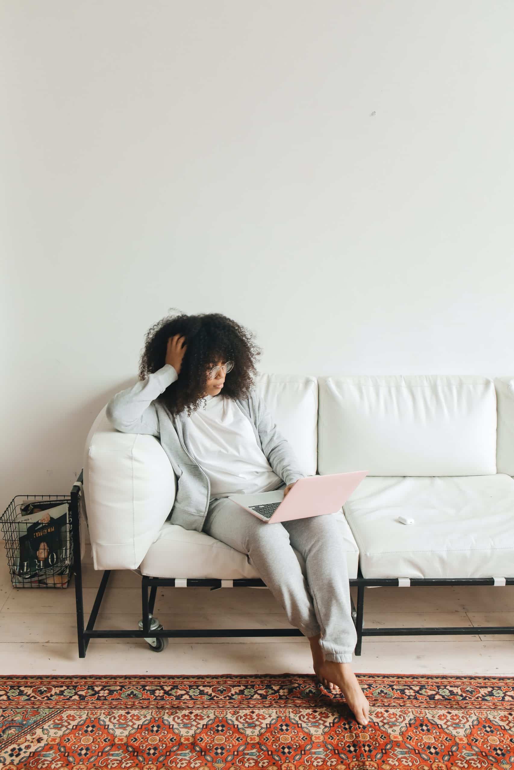 Woman sitting on white sofa, a pink laptop on her lap