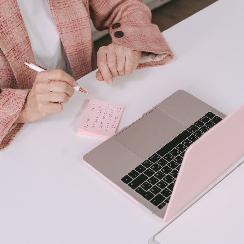 Person writing notes beside laptop.